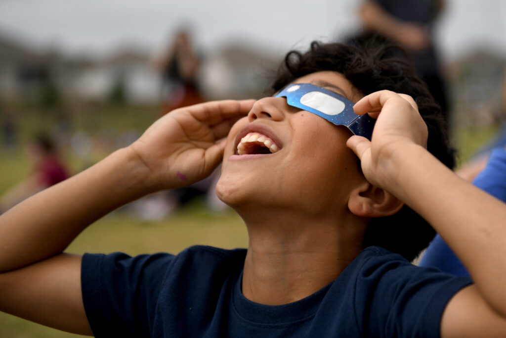 A student wearing safety glasses stares up at the eclipse event