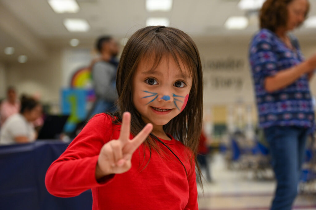 Child with face paint giving the peace sign to the camera