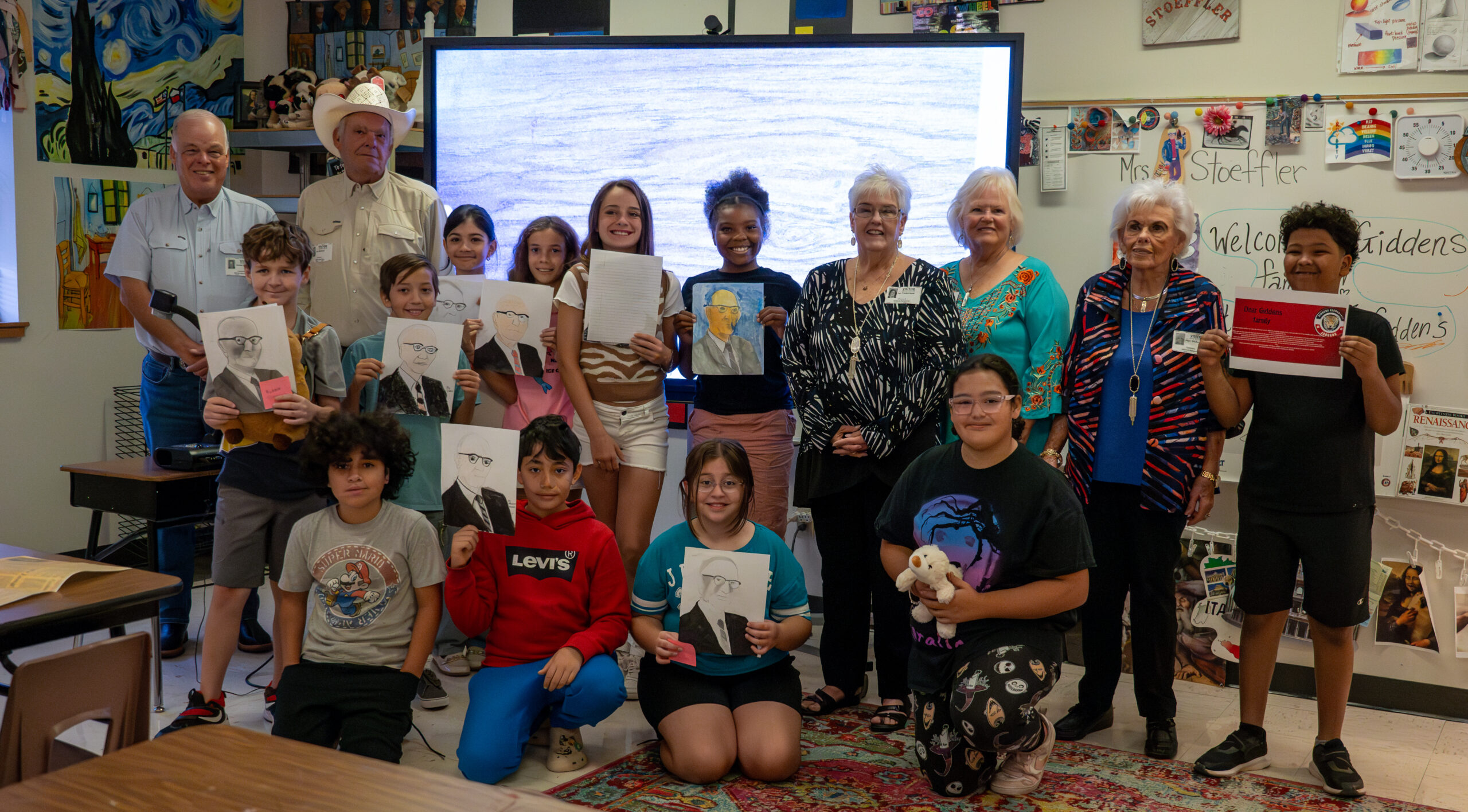 5th-grade students pose with the Giddens family and the portraits they drew of Lois Giddens
