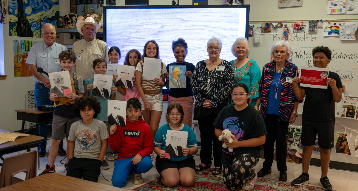 Members of the Giddens family pose with 5th-grade students at Giddens Elementary School, who hold up portraits they drew of Mr. Lois Giddens, the school's namesake.