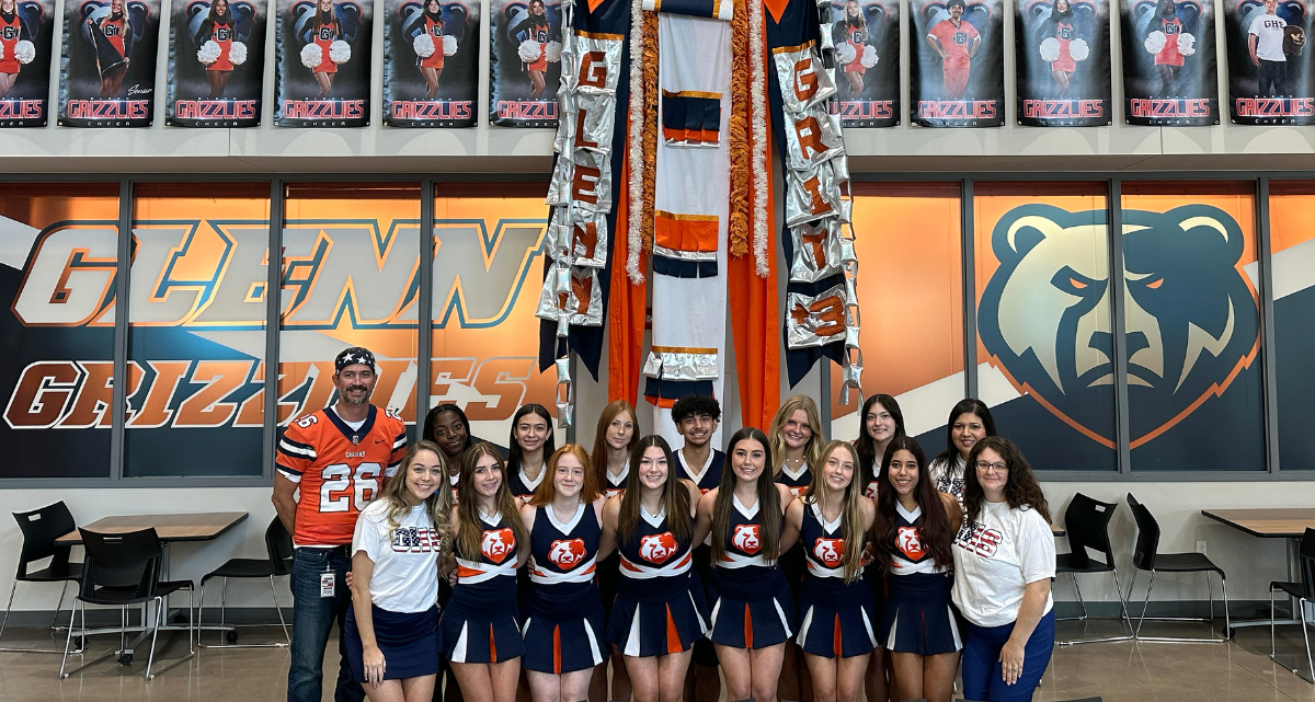 The Glenn High School varsity cheer team, coaches, principal, and attendance clerk pose for a group photo with the school's Texas-sized mum.